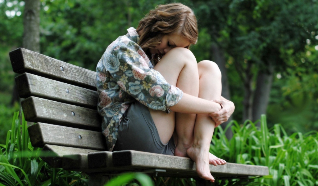 Девушка грустит сидя на скамье