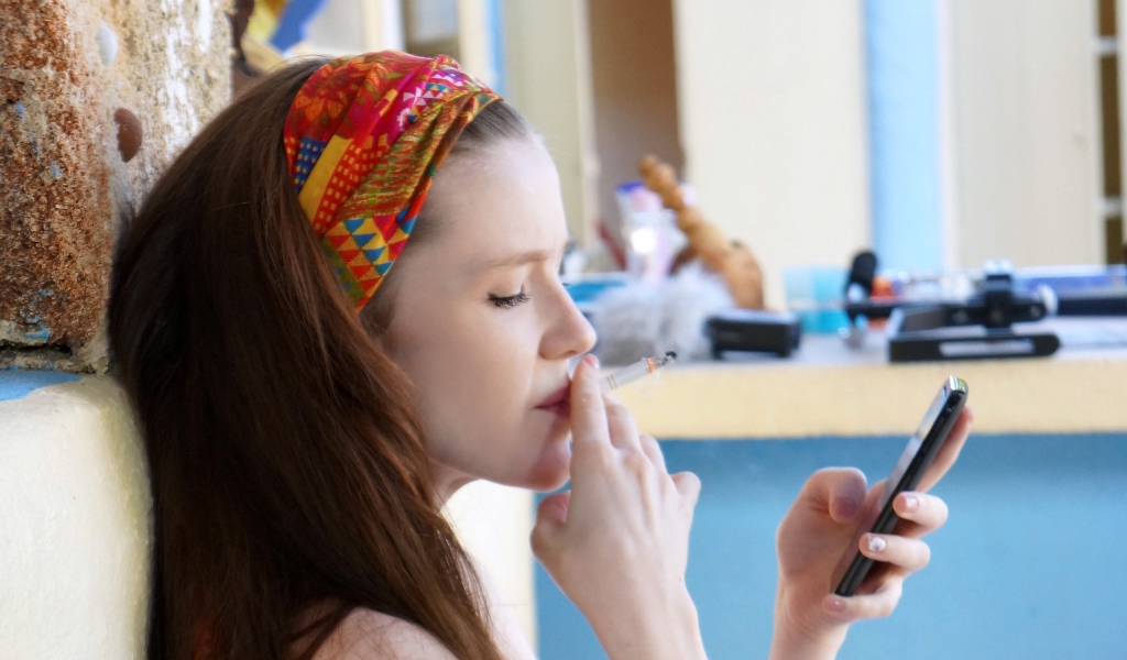 Девушка курит и смотрит на экран телефона