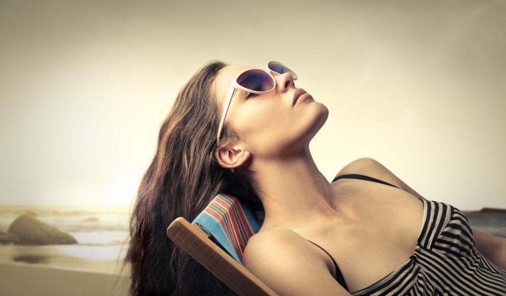 Девушка в очках загорает в шезлонге
