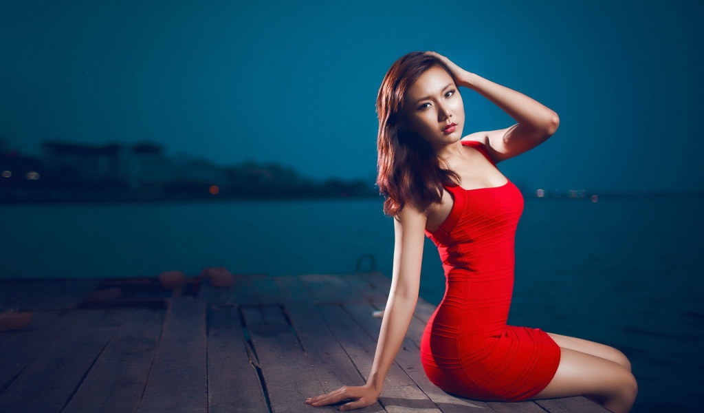 The girl in the red dress sitting on the edge of a wooden jetty