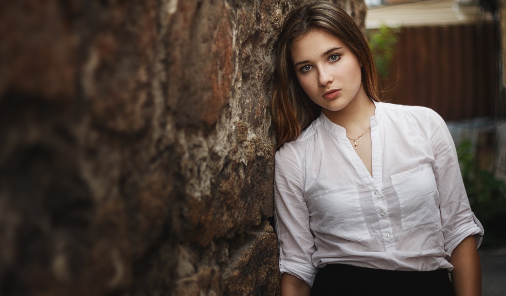 Девушка в белой рубашке стоит у стены