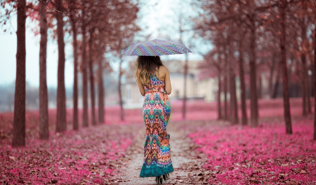 Девушка под зонтом в красивом платье идет по аллее