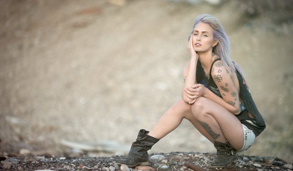 Девушка с татуировками в форме цветов сидит на корточках
