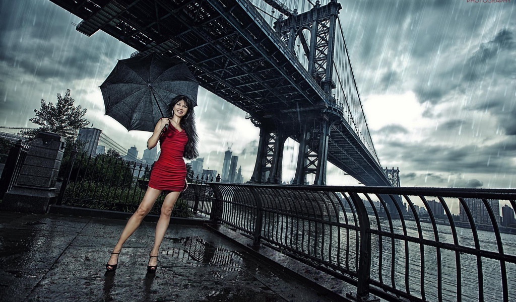 Модель в красном платье с зонтом стоит под мостом