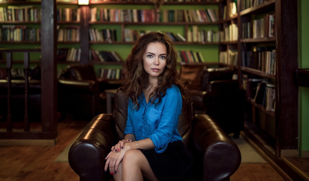 Модель в голубой блузке сидит на кожаном кресле