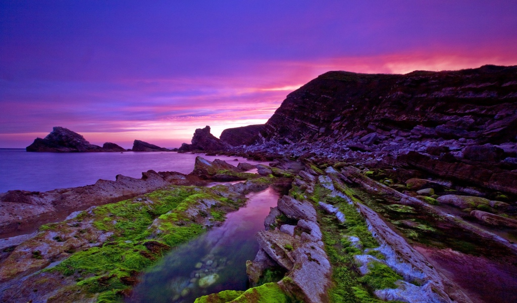 Голые скалы у берега на фоне сиреневого заката