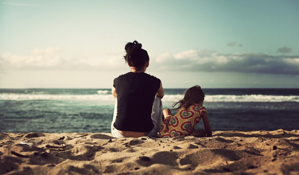Женщина с дочкой сидят на песке на берегу моря