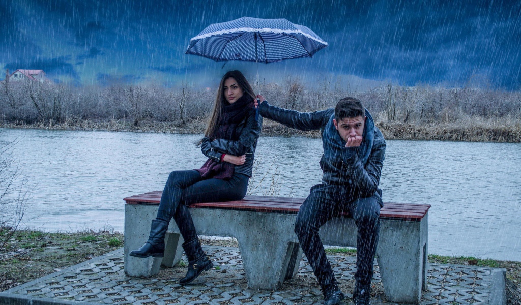 Парень держит над девушкой зонт во время дождя