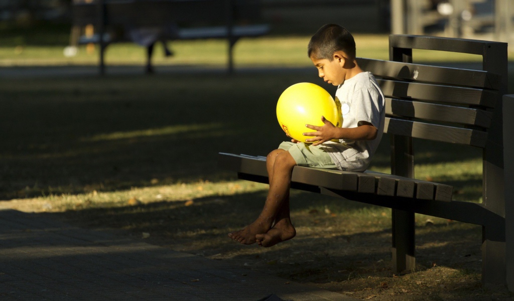 Мальчик сидит на скамье с шариком в руках