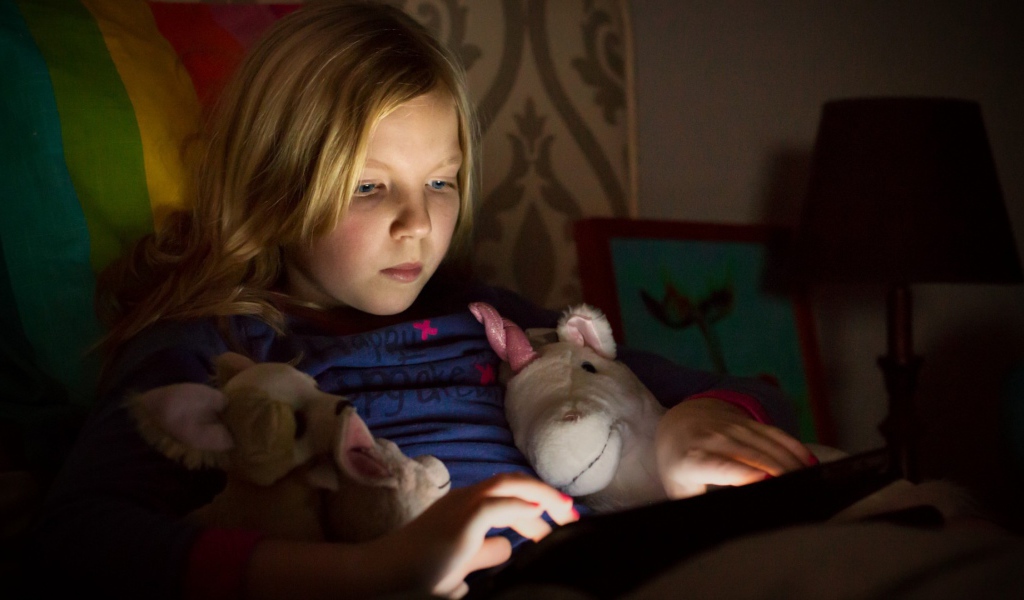 Девочка играет с планшетом лежа в кровати