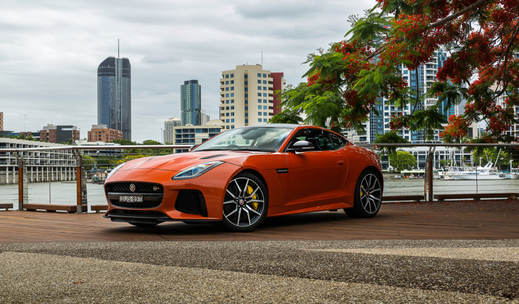 Оранжевый автомобиль Jaguar F-Type на фоне небоскребов 