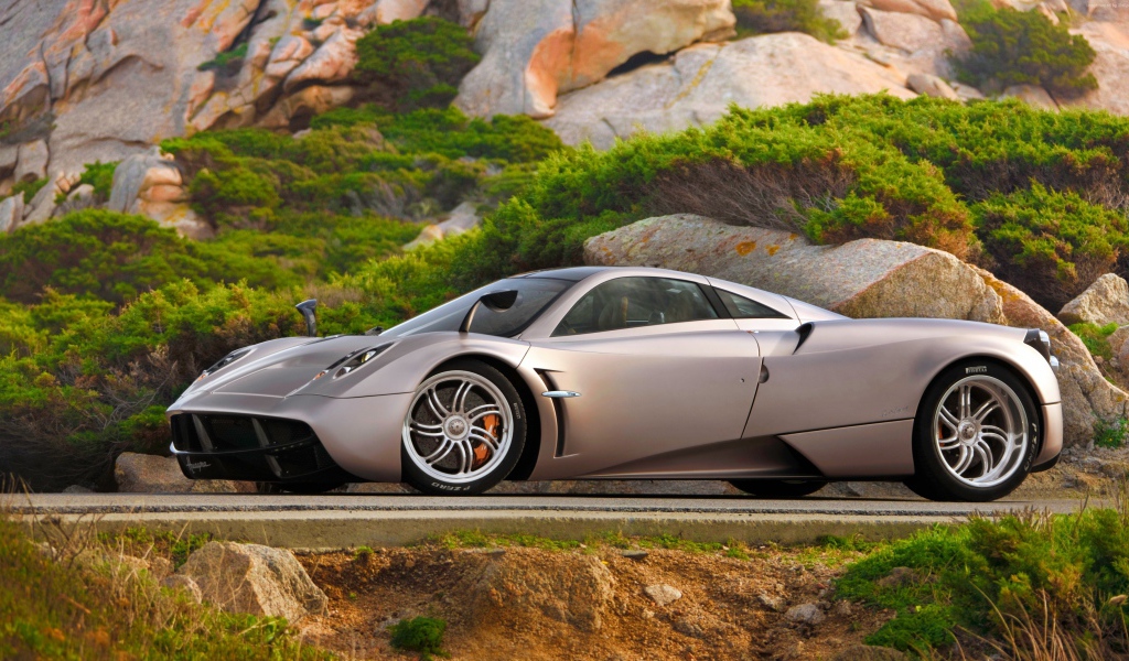 Серебристый быстрый автомобиль  Pagani Huayra на трассе у скалы