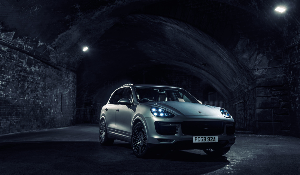 Серебристый автомобиль Porsche Cayenne в тоннеле с включенными фарами