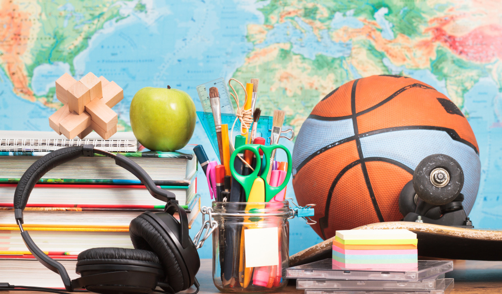 Мяч, наушники, книги и канцелярские принадлежности на столе на фоне карты