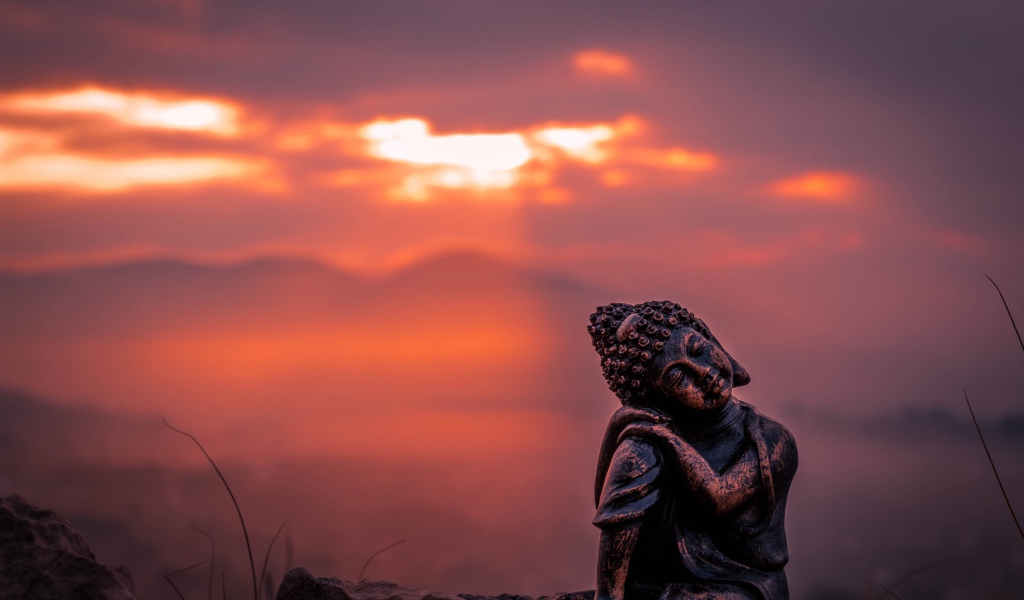 Статуя Будды на фоне солнца на закате