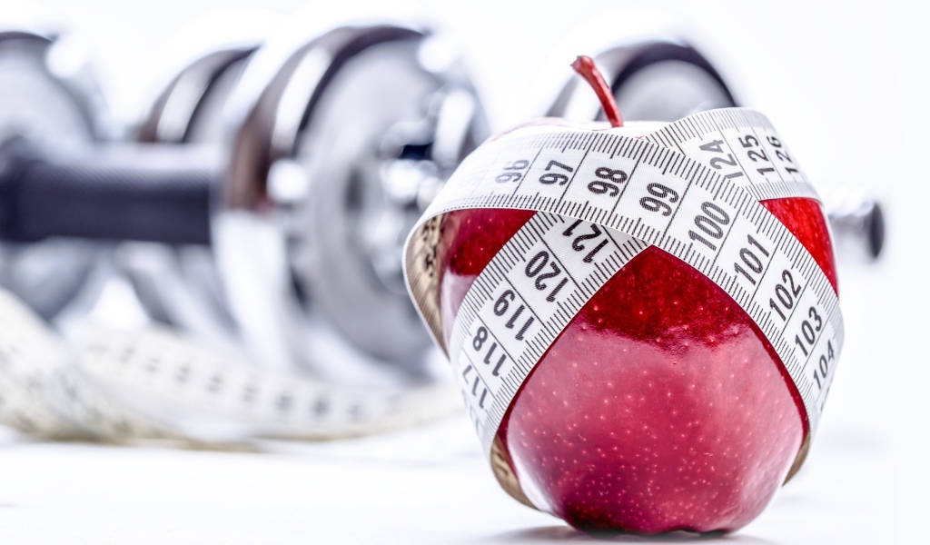 Красное яблоко перемотано мерной лентой и гантели на белом фоне