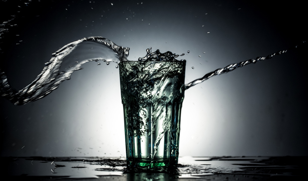 Брызги воды из стакана с водой на сером фоне