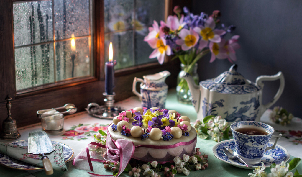 Красивый торт на столе с сервизом и горящей свечой у окна