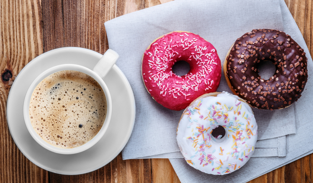 Чашка кофе с тремя аппетитными пончиками на столе