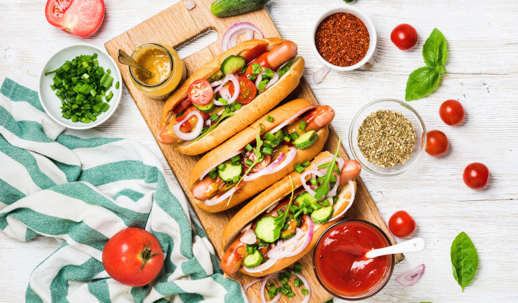 Аппетитные хотдоги на разделочной доске с овощами
