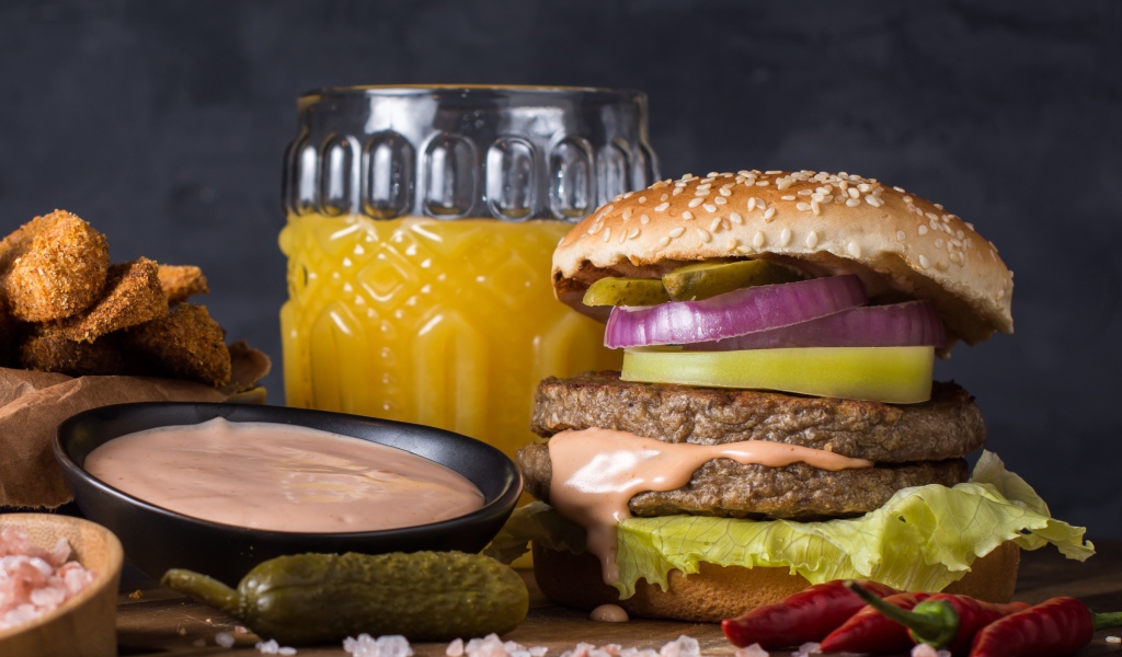 Аппетитный гамбургер на столе с соусом, овощами и соком