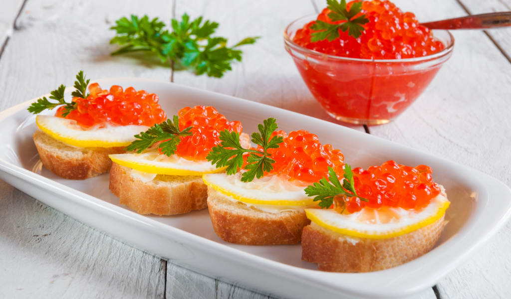 Бутырброды с красной икрой и лимонами на белой тарелке