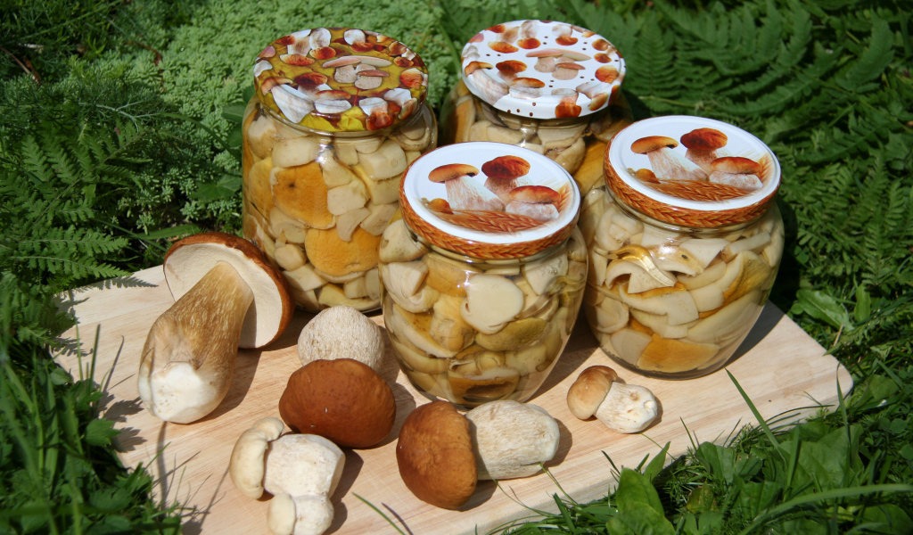 Консервированные грибы в банках на разделочной доске со свежими