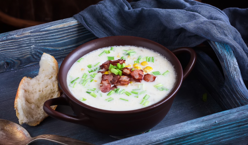 Сырный суп с зеленью и беконом на столе с куском хлеба