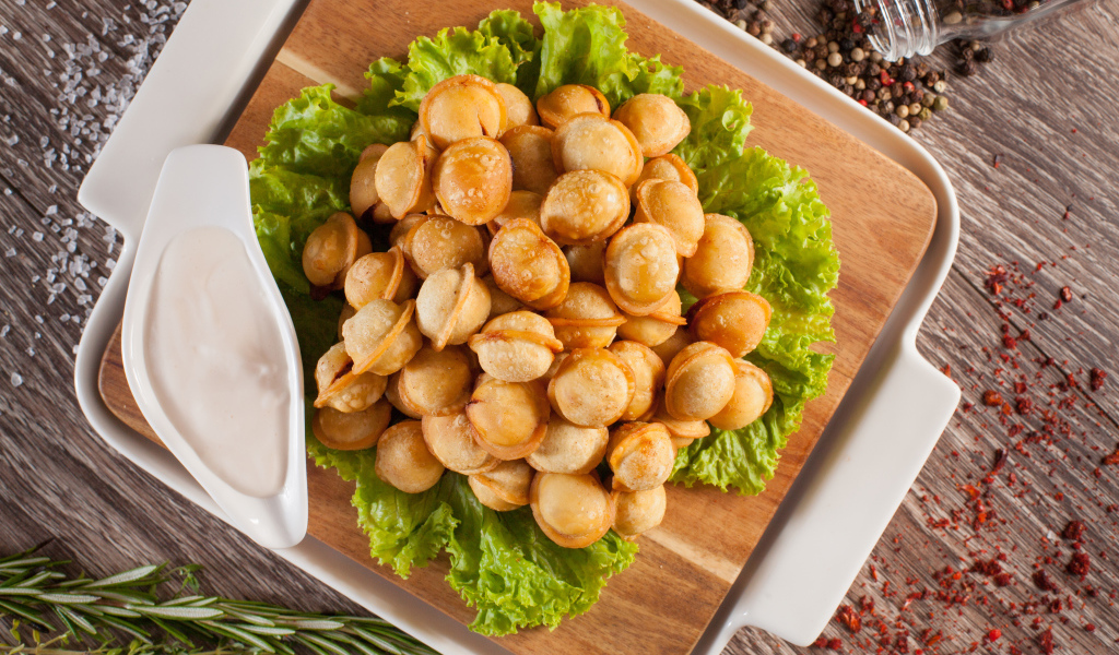 Пельмени с соусом и листьями салата лежат на разделочной доске