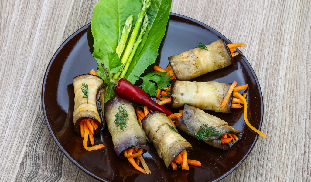 Рулетики из баклажанов с морковью на тарелке с листьями салата