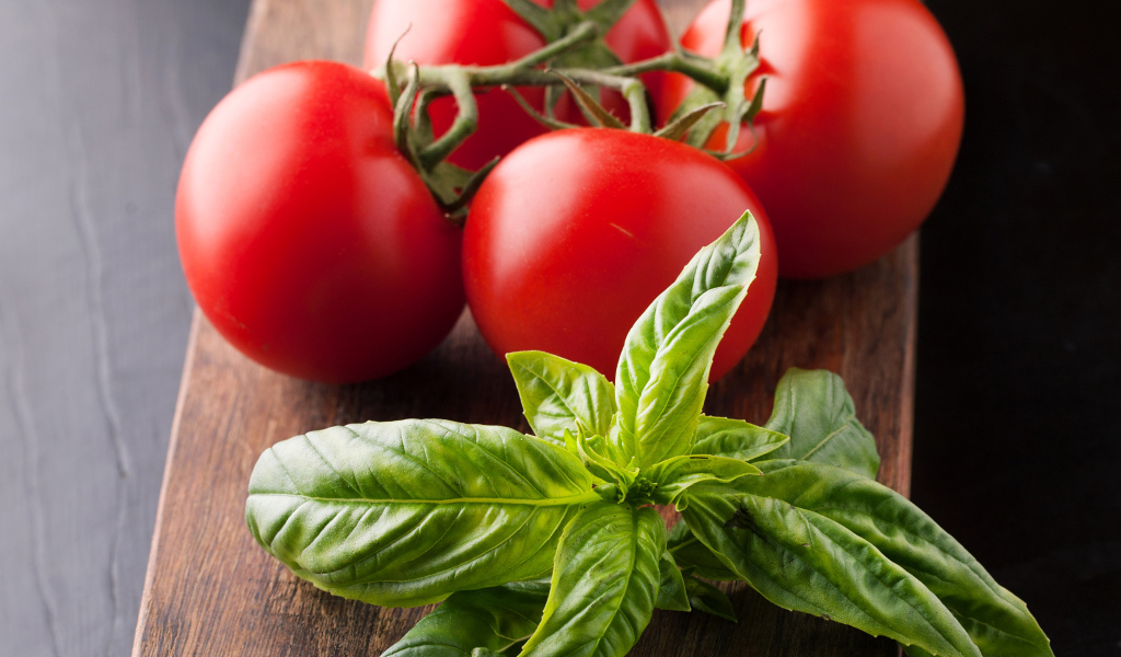 Свежие помидоры на разделочной с зеленью