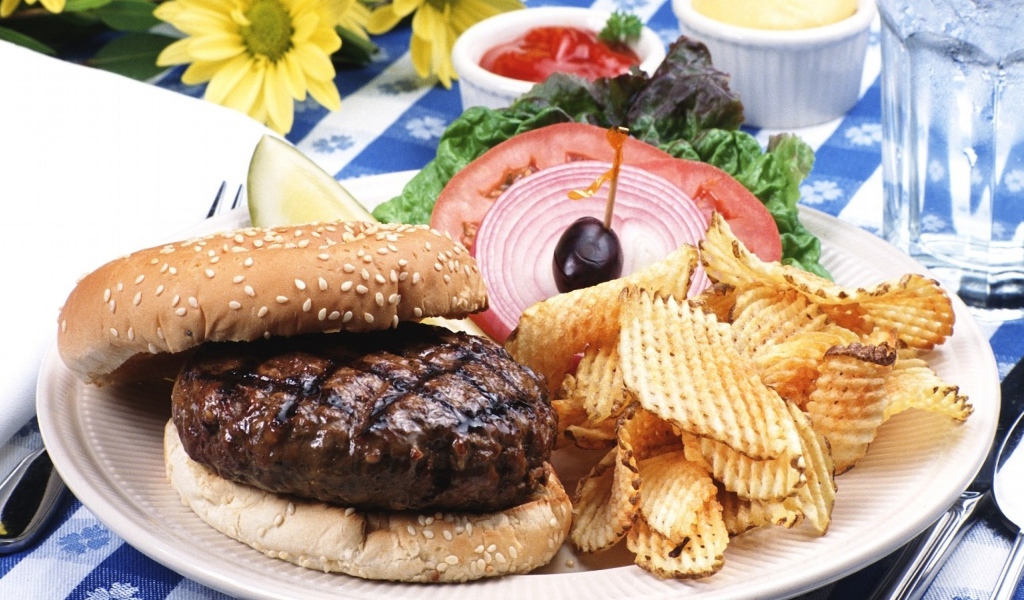 Гамбургер с котлетой и картофельные чипсы на тарелке с овощами