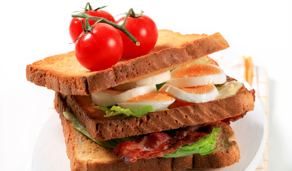 Сэндвич с беконом, яйцами и овощами на белом фоне