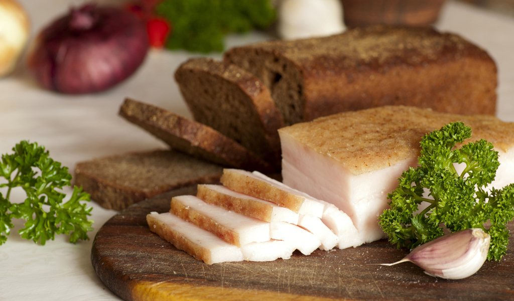 Нарезанное кусочками сало и черный хлеб на разделочной доске