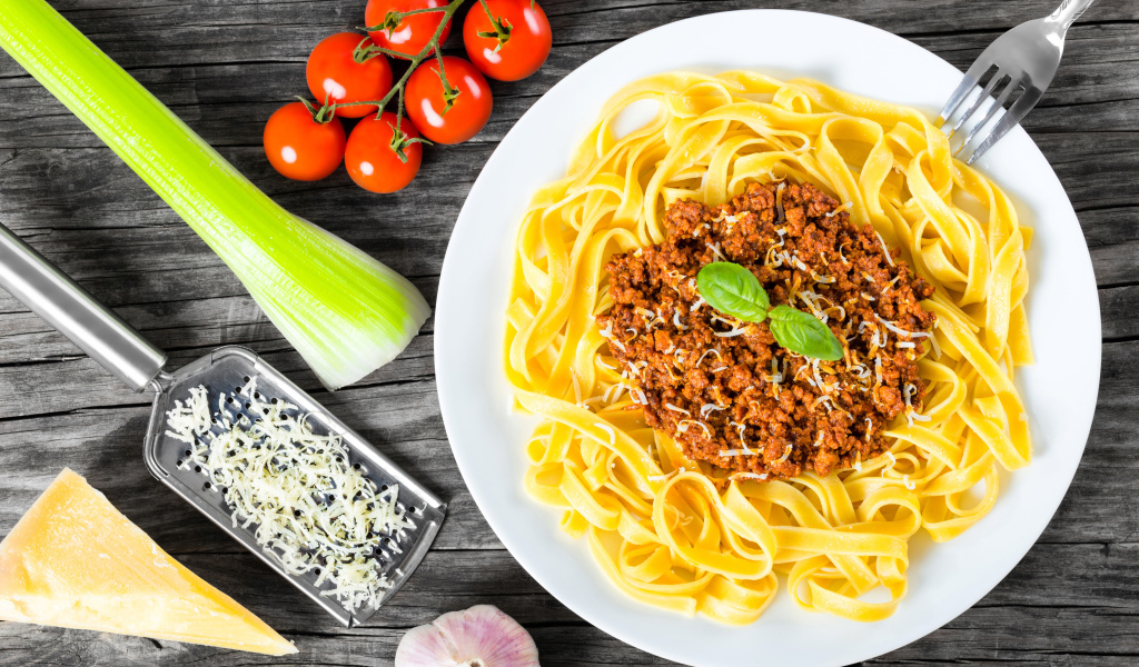 Спагетти на белой тарелке с мясом и сыром
