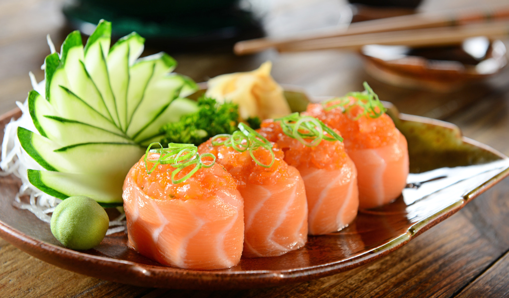 Суши из красной рыбы на тарелке со свежими огурцами и зеленью