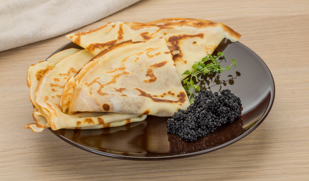 Тонкие блины на тарелке с черной икрой