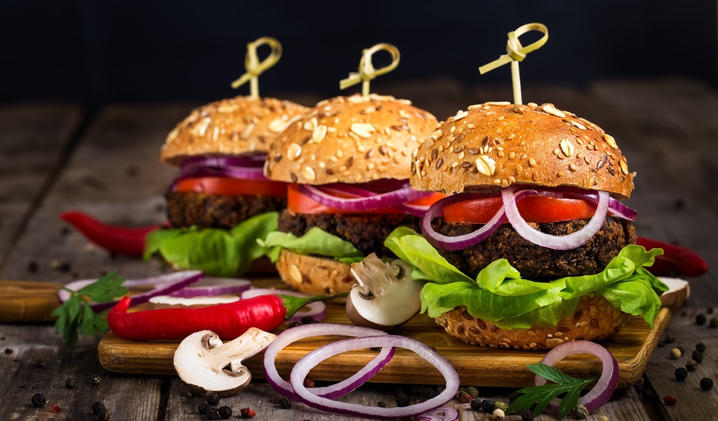 Три аппетитных гамбургера с кольцами лука и перцем