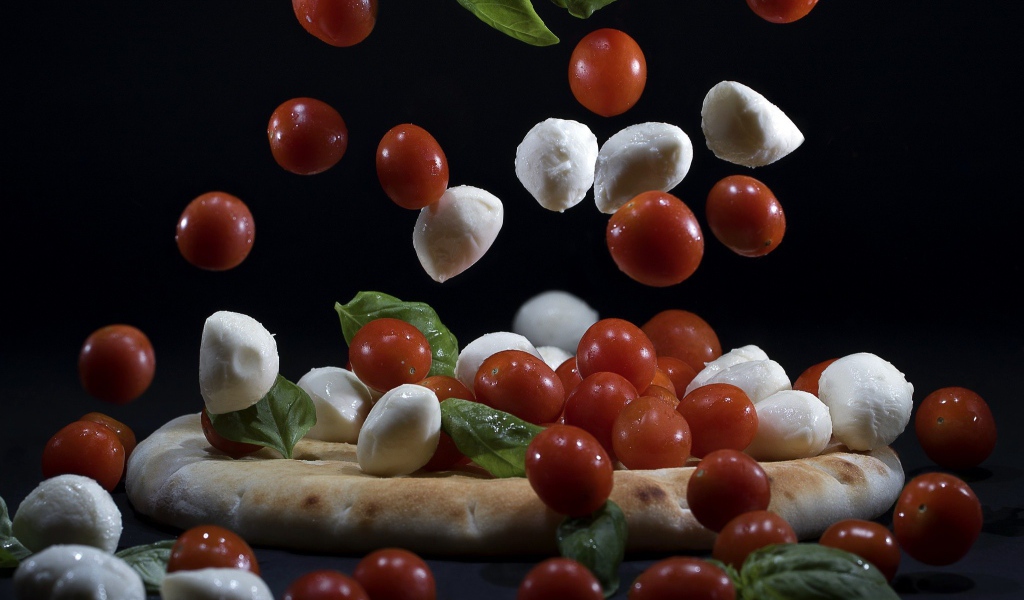 Помидоры и сыр Моцарелла падают на пиццу 