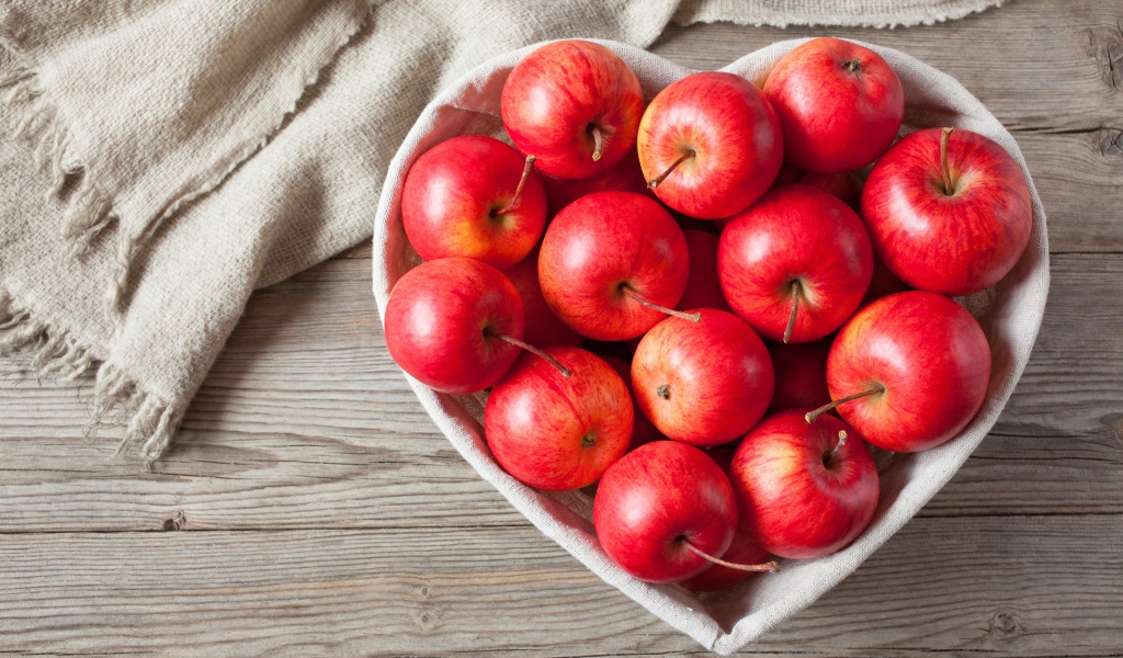 Красивые красные яблоки в тарелке в форме сердца на столе