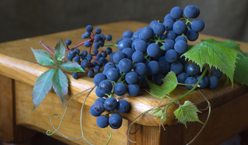 Blue grapes with green leaves lie on a wooden table