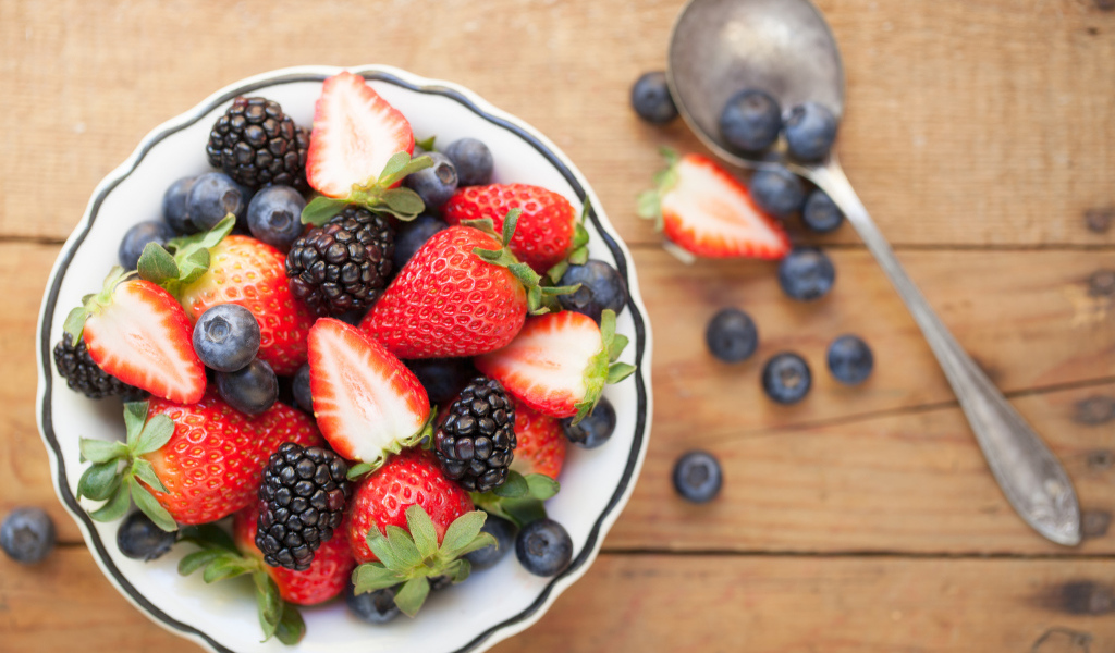 Свежие ягоды клубники, черники и ежевики в тарелке на деревянном столе