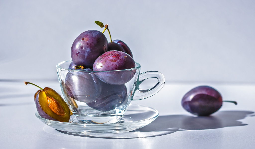 Спелые синие сливы на столе в стеклянной чашке