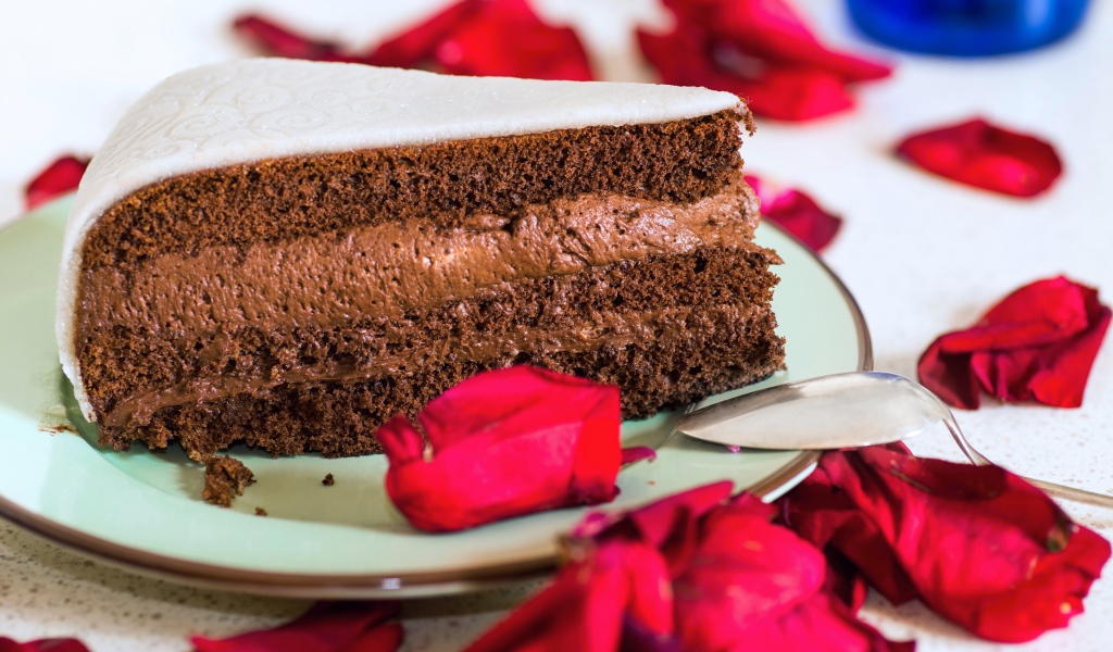 Кусок торта с шоколадным кремом и красными лепестками розы