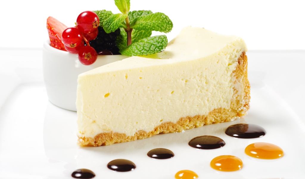 Кусок чизкейка на белой тарелке с ягодами и мятой