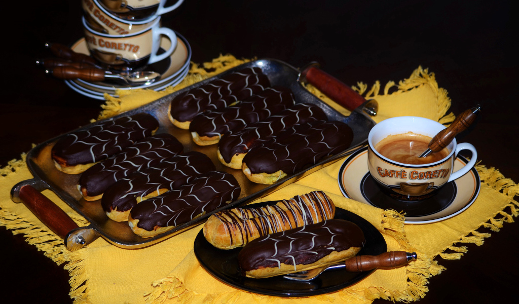 Аппетитные сладкие эклеры с шоколадом и чашками кофе на столе