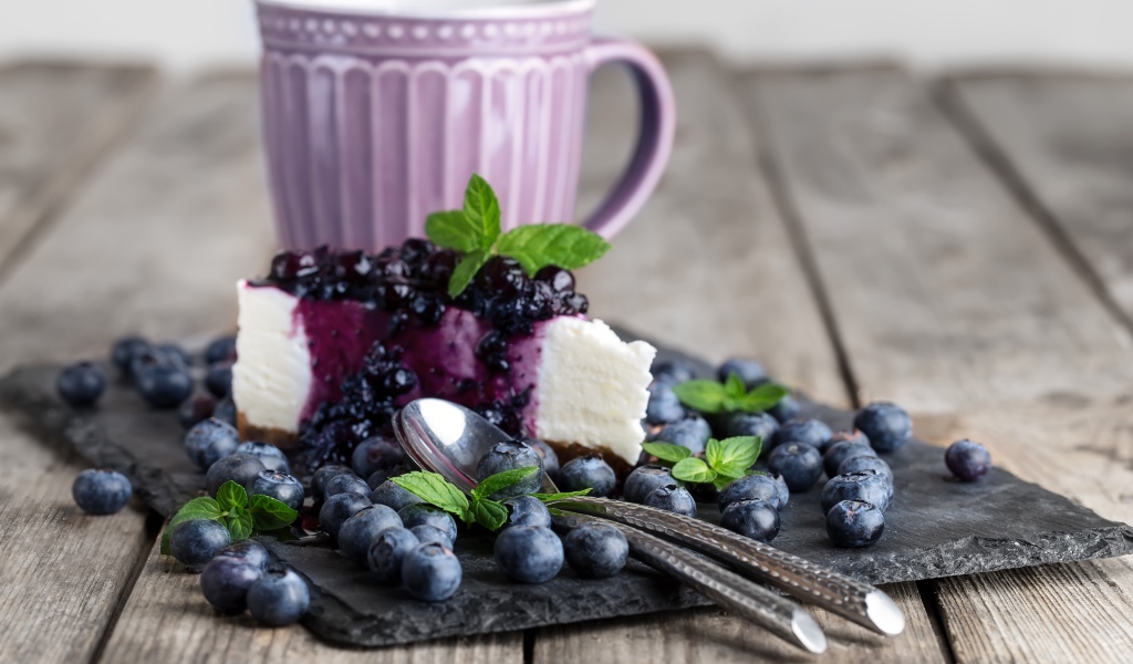 Черничный чизкейк со свежими ягодами лежит на столе с чашкой