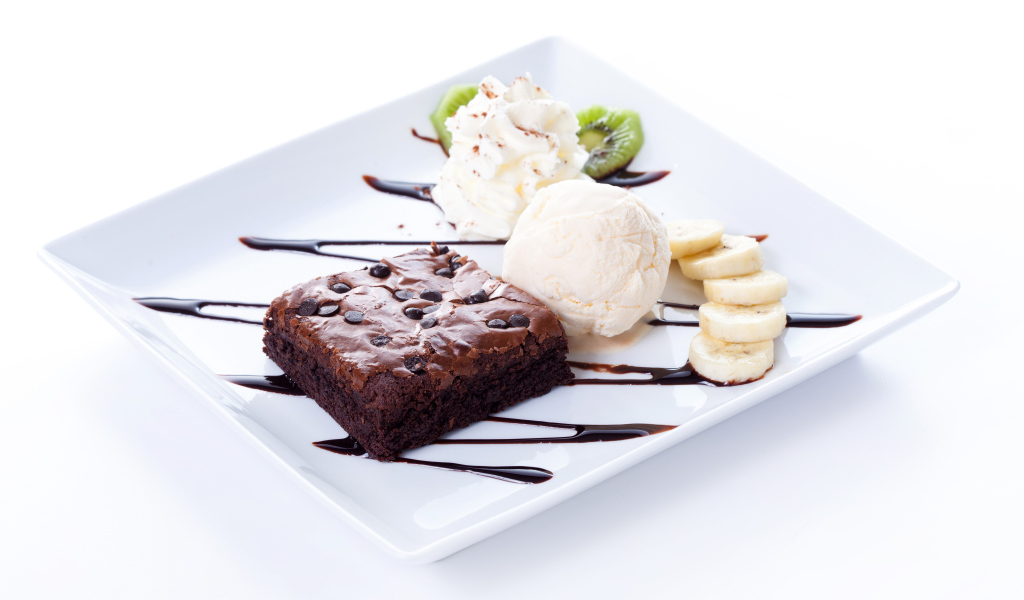 Шоколадное пирожное с мороженым, сливками и кусочками банана на белой тарелке