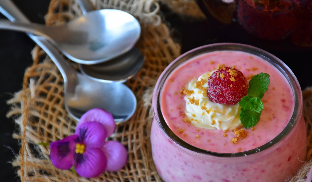 Десерт с малиной и кремом на столе с ложками