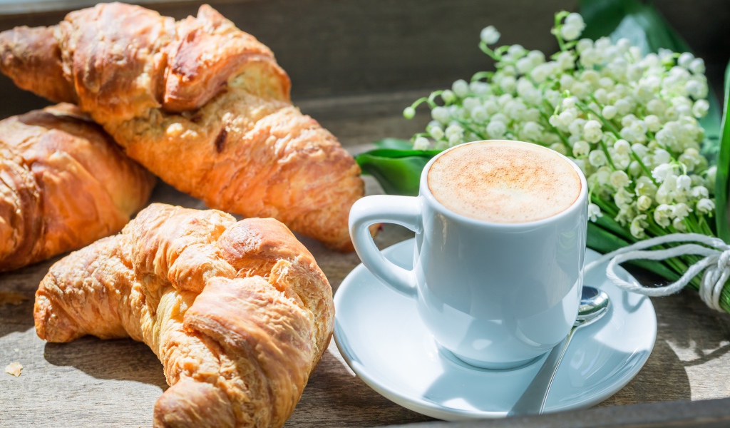 Свежие круассаны с чашкой кофе и букетом ландышей на столе